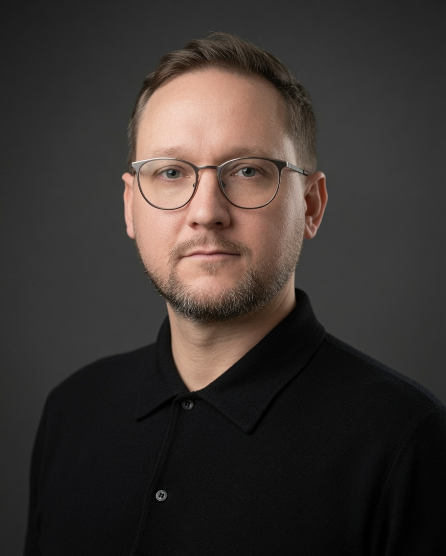 Portrait photo of Dan Hesketh: glasses, a black shirt, a dark grey background.